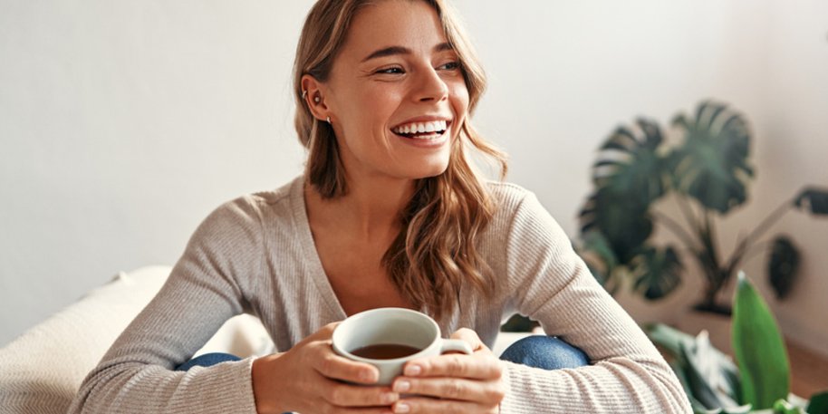 A smiling woman holding a mug on a couch.